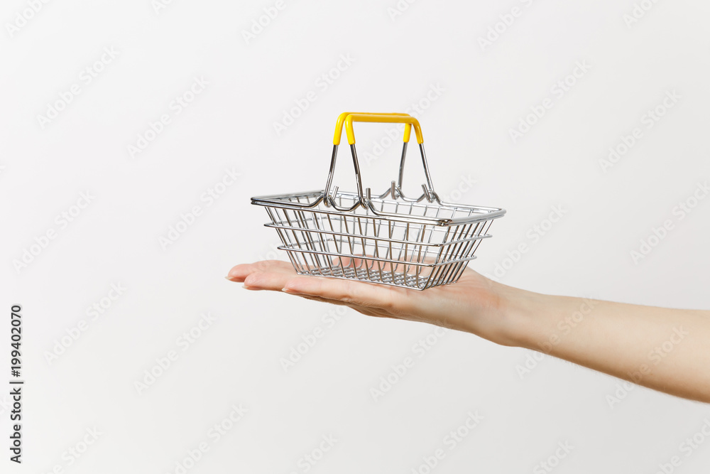Close up of female hand horizontal holds toy metal shopping basket with yellow plastic handle isolated on white background. Shopping concept. Copy space for advertisement.