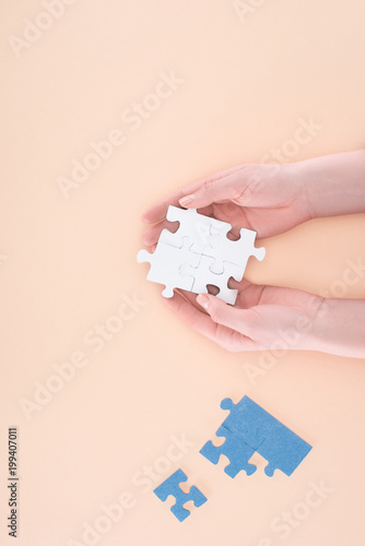 cropped image of businesswoman holding assembled puzzles piece in hands isolated on beige, business concept