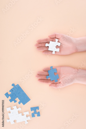 cropped image of businesswoman holding blue and white puzzles in hands isolated on beige, business concept