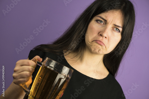 Cute Brunette Girl on a Purple Background Shows shis Dislike to Pint of Beer