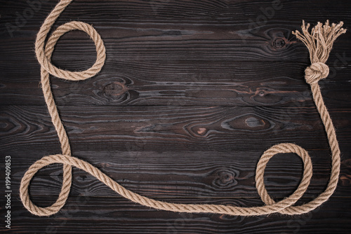 Fototapeta Naklejka Na Ścianę i Meble -  top view of brown nautical rope with knot on dark wooden surface