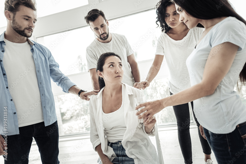 Obraz premium Thank you. Cheerless unhappy young woman sitting on the chair and looking at her friend while taking a glass of water