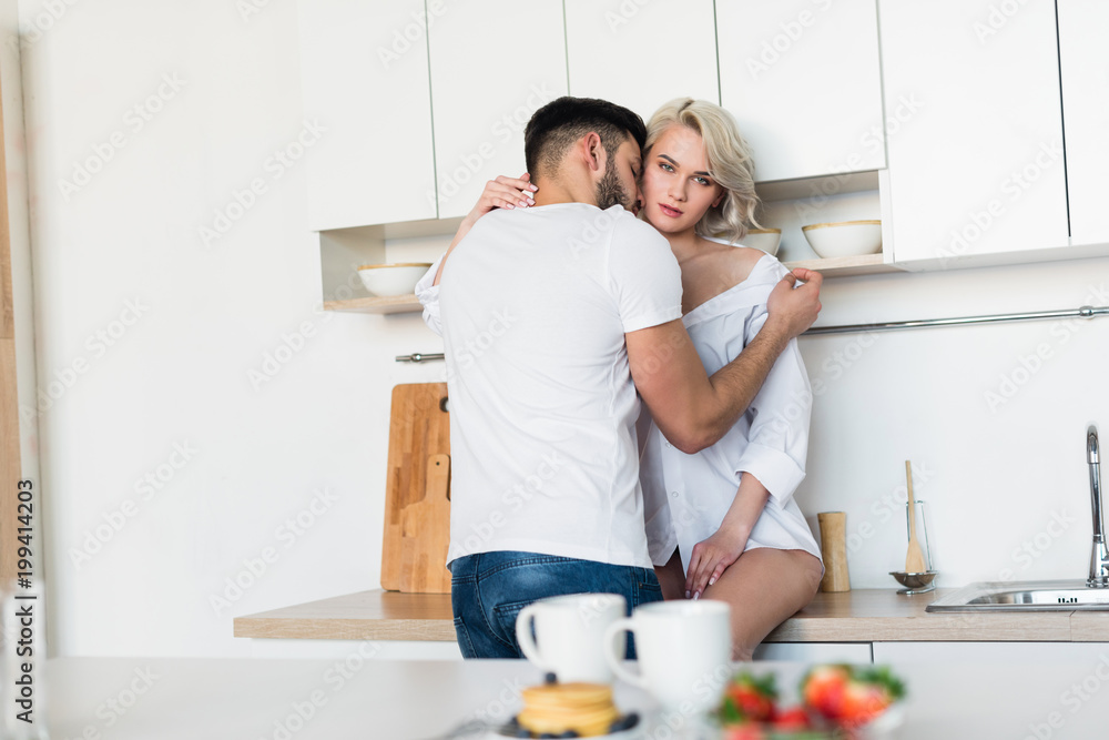 young man hugging and kissing sexy girlfriend, girl looking at camera in kitchen young man hugging and kissing sexy girlfriend, girl looking at camera in kitchen