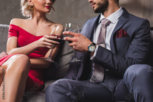 cropped shot of couple in suit and evening gown holding glasses of red wine