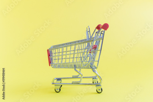 Closeup of tiny shopping cart on yellow background