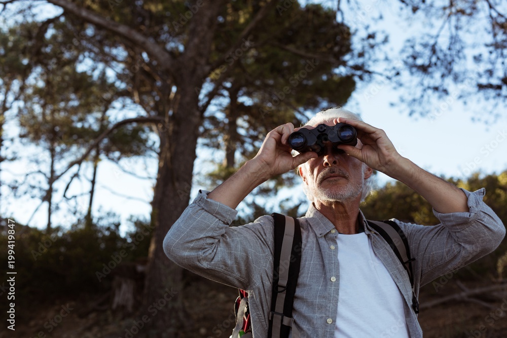 Senior hiker looking through binoculars in forest Senior hiker looking through binoculars in forest