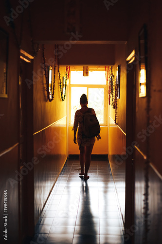 The girl with the keys in her hand walks along the dark corridor back lit with natural light.