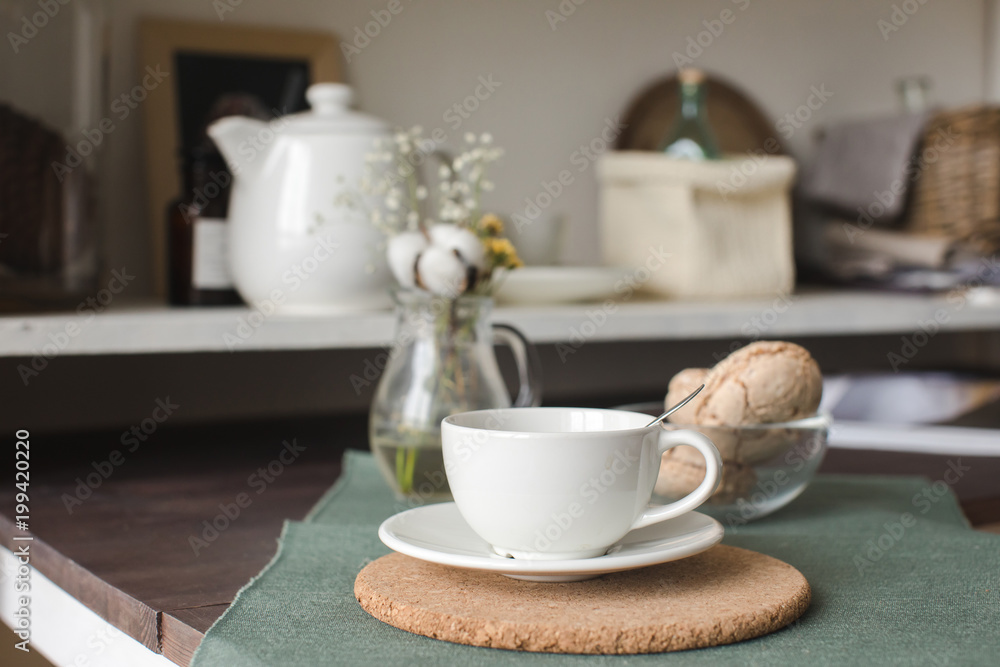 Arranged white cup on table with biscuits and kitchen utensil on background. 