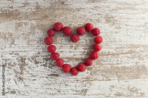 Heart made of raspberries on white wooden background.