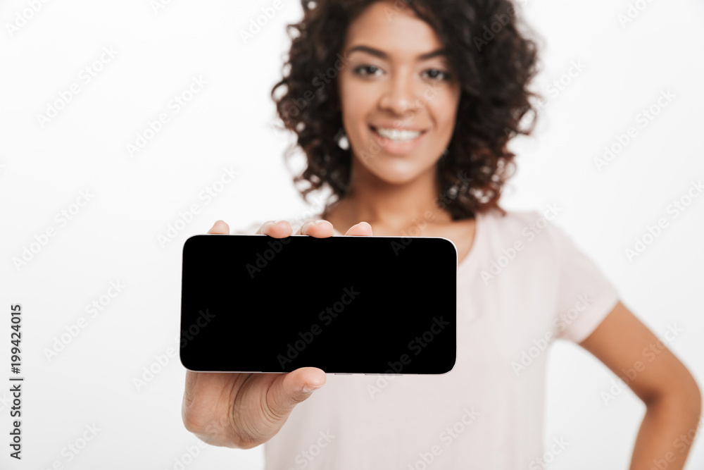 Brunette woman with afro hair doing commercial and demonstrating copyspace screen of smartphone on camera, isolated over white background