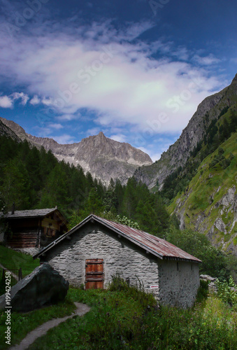 beautiful lush mountain valley with old cottages and high alpine peaks behind © makasana photo