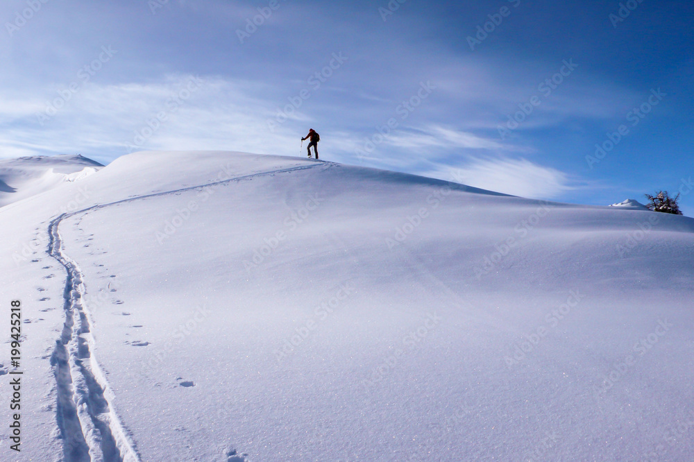 a backcountry skier hiking along a mountain ridge towards the summit near Klosters in the Swiss Alps in deep winter