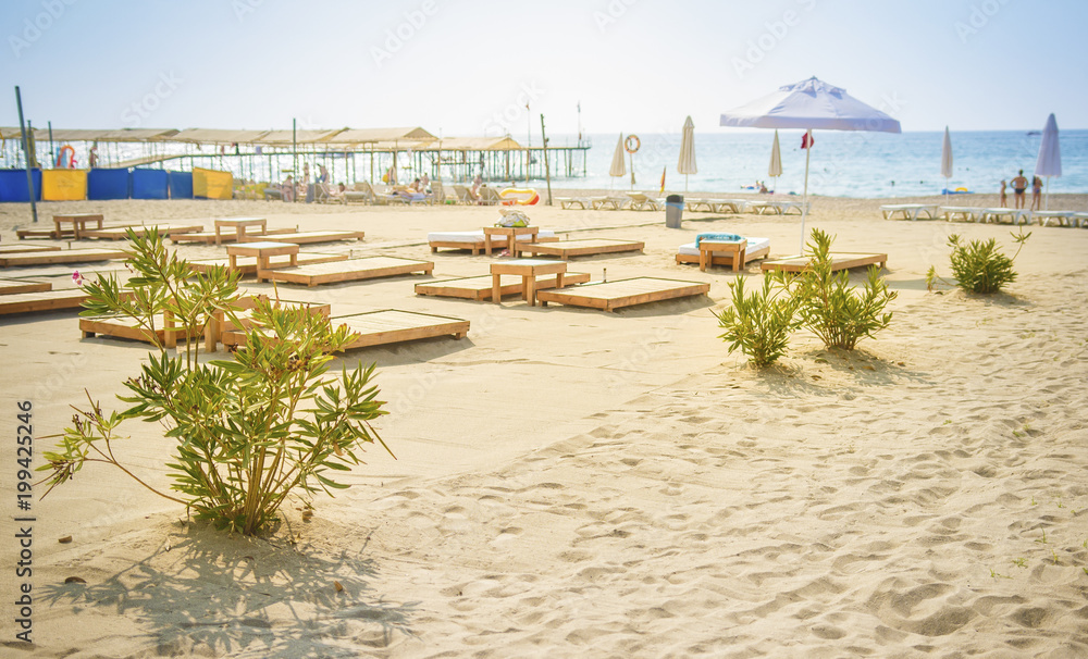 Sandy beach on blue sea background. Umbrellas and deck chairs on shore of sea. Summer day on beach rest. Vacation concept. View on sea beach in sunny clear day in Turkey Konakli. Sandy beach on blue sea background. Umbrellas and deck chairs on shore of sea. Summer day on beach rest. Vacation concept. View on sea beach in sunny clear day in Turkey Konakli.