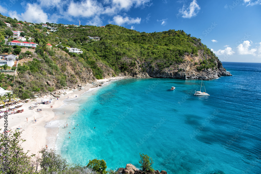 Naklejka premium Harbor with sand beach, blue sea and mountain landscape in gustavia, st.barts. Summer vacation on tropical beach. Recreation, leisure and relax concept. Wanderlust and travel with adventure.