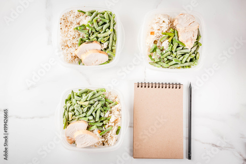 Food control, diet concept, orthorhysis. Healthy balanced meals, homemade lunches for work, office with rice, vegetables, chicken fillet. Notepad for the diet plan. White marble table, Top view photo