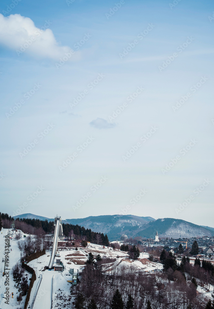 Mountain wintersport scenery with ski-jump under blue cloudy sky. Winterberg, Germany.