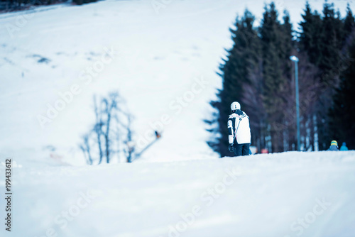 Skier in white protective helmet and jacket going downhill. Rear view.