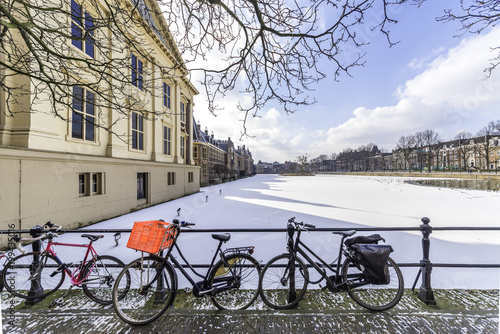 Rusty bicycles in front of the panoramic view of the Dutch parliament building and its frozen pond water