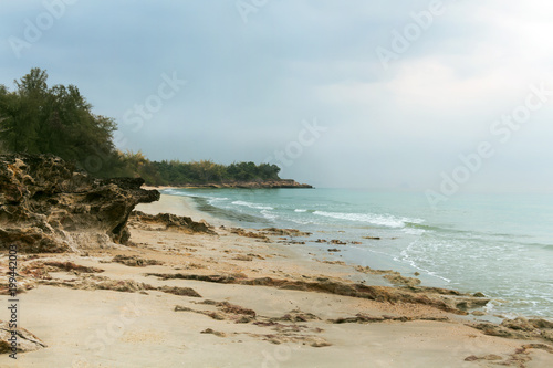 Sunshine in the morning with sea waves slowly a the splashing on the sand and rocks with moss in the sea. Tranquil idyllic scene of the tropical beach.