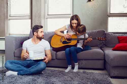 The family plays guitar together and sings songs. Mother, father and daughter spend time together.