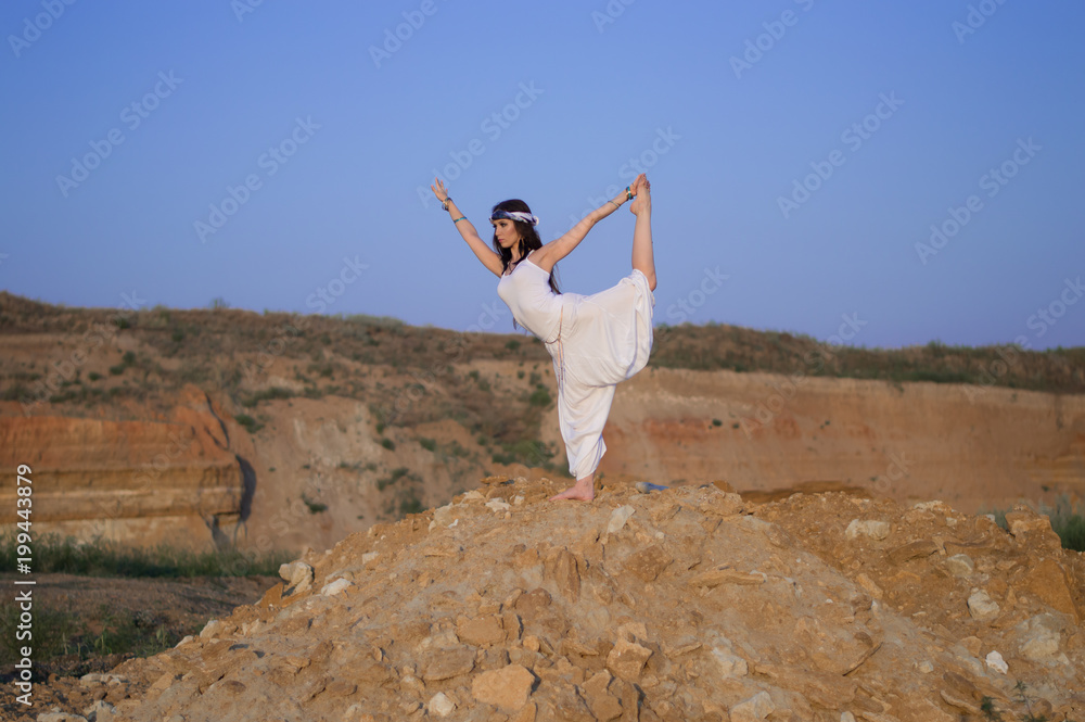 Girl in white clothes doing yoga in nature. Mountainous terrain. Blue sky. Green grass. Girl in white clothes doing yoga in nature. Mountainous terrain. Blue sky. Green grass.