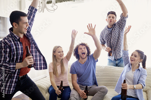 A group of friends at a party cheerfully raise their hands up in the room.