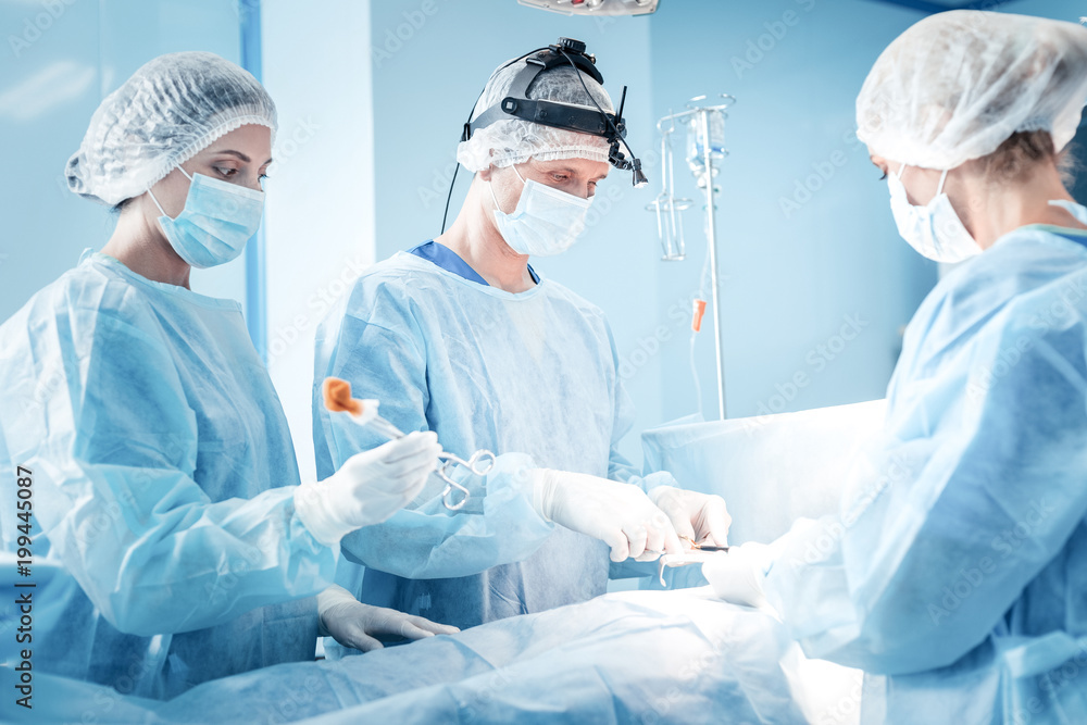 Difficult operation. Professional smart serious surgeons wearing medical uniform and working while performing a difficult operation Difficult operation. Professional smart serious surgeons wearing medical uniform and working while performing a difficult operation