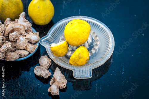 Raw fresh ripe lemons or Citrus × limon in a glass squeezer on black wooden surface in dark Gothic colors with ayurvedic herb dried ginger it helps in digestion,relief of cough, it is antifungal herb. photo