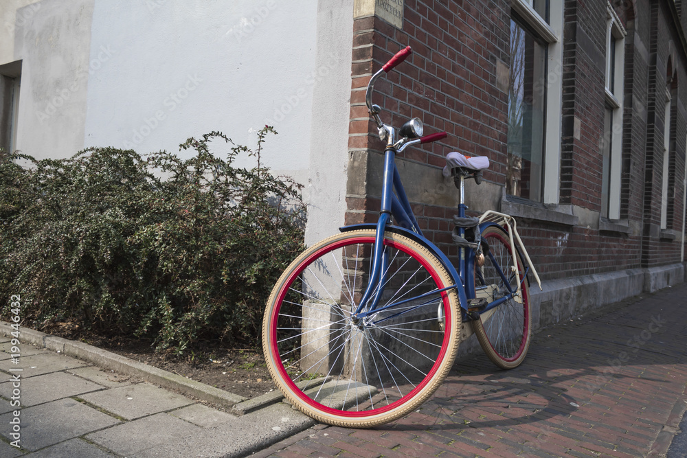 blue bicycle next to a wall of duch house with white and red  tires
