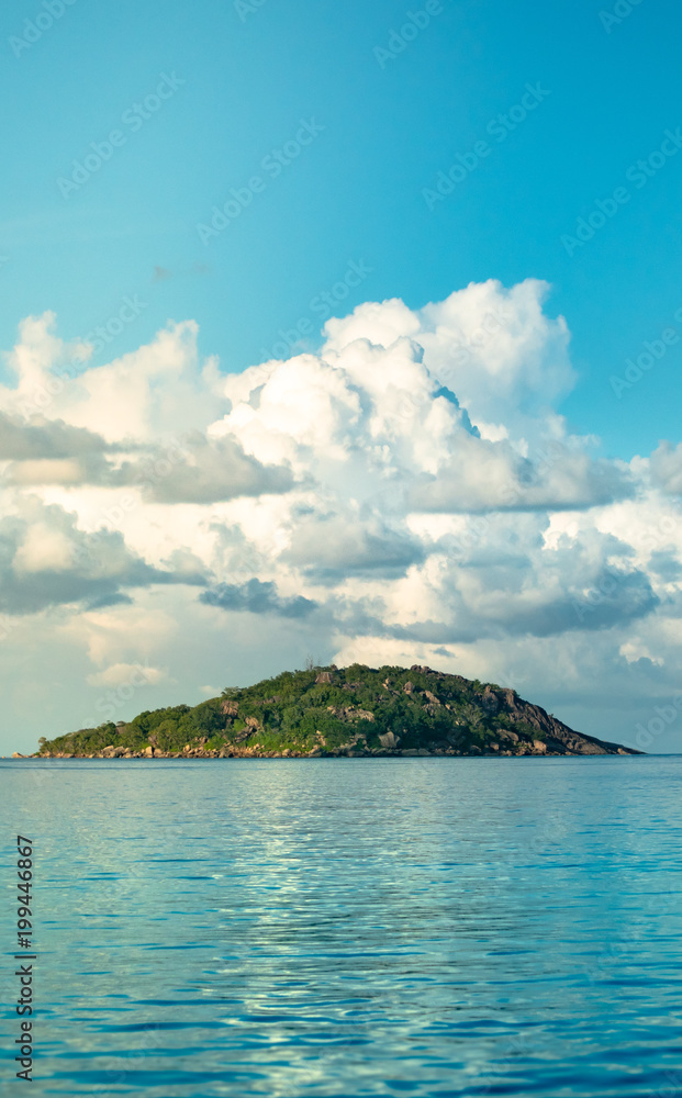 Low angle of a rocky green island with large cloud formations in the distance in the Seychelles