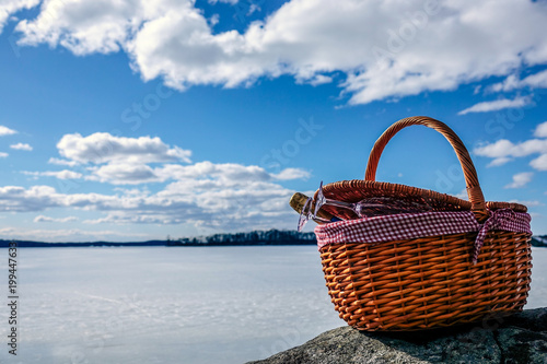Pic nic basket with champagne glass and bottle on a cliff. Sunny cold day with a frozen lake in the background and a beautiful blue sky with white fluffy clouds. photo
