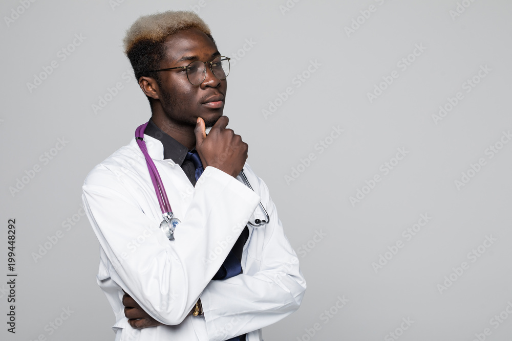 Portrait of handsome pensive Afro American doctor in white coat keeping hand on his chin, looking away and thinking, isolated on gray background Portrait of handsome pensive Afro American doctor in white coat keeping hand on his chin, looking away and thinking, isolated on gray background
