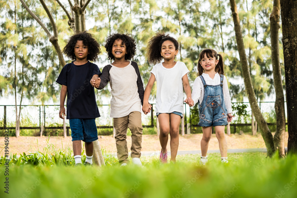 Fototapeta premium Group of children having fun playing together. Kids holding hands and walking in a park.