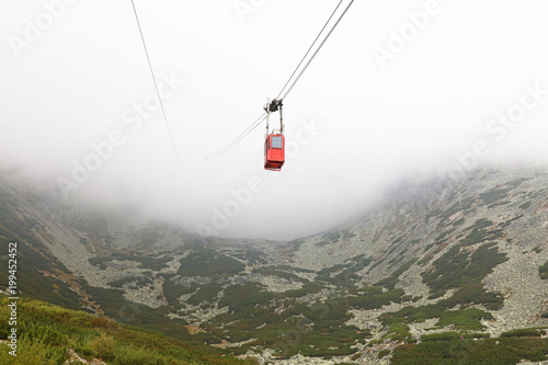 Red mountain cableway car in clouds and fog