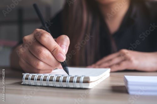 Closeup image of a woman's hand writing down on a white blank notebook on table