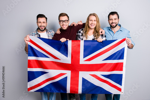 Cheerful excited delightful attractive men wearing casual checkered jeans denim shirt outfit holding with hands jack union flag isolated on gray background