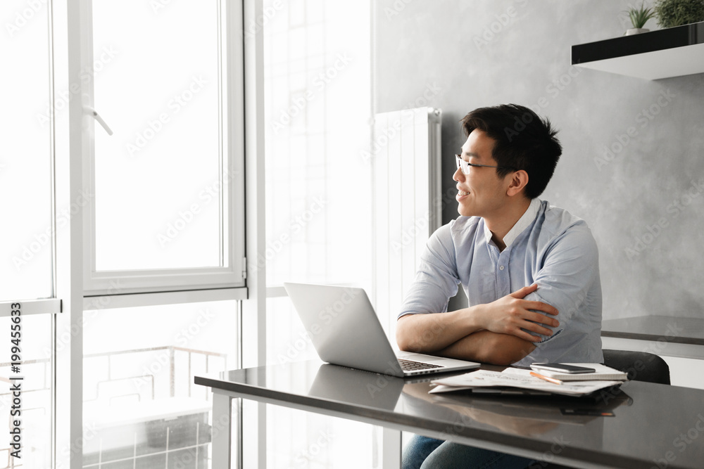 Fototapeta premium Portrait of a happy young asian man working on laptop