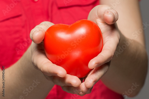 A girl holds a red heart in her hands on a gray background