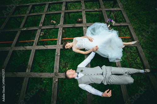 beautiful fabulous happy bride and stylish groom lying down on the grass on the background of the sunny stunning mountains