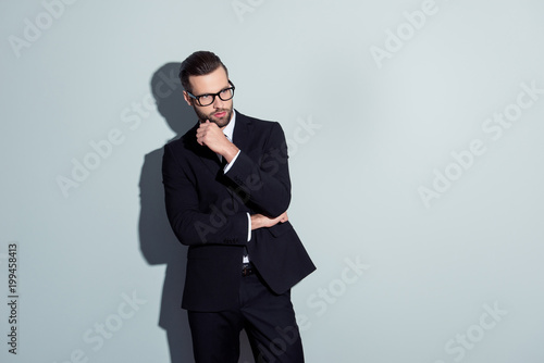 Stunning, perfect, manly, virile, harsh man in black suit, suspects something, having doubts, holding hand near face, touching bristle, looking to the side, isolated on grey background