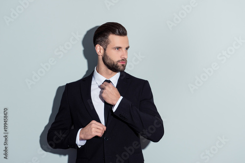 Portrait of attractive, cool, virile, harsh, manly business person in classic outfit correcting tie, prepare for important meeting, looking to the side, isolated on grey background