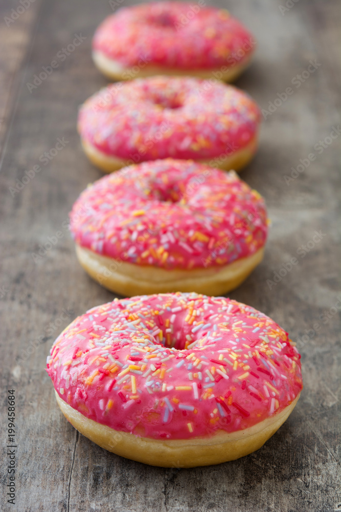Pink frosted donut with colorful sprinkles on wooden table Pink frosted donut with colorful sprinkles on wooden table
