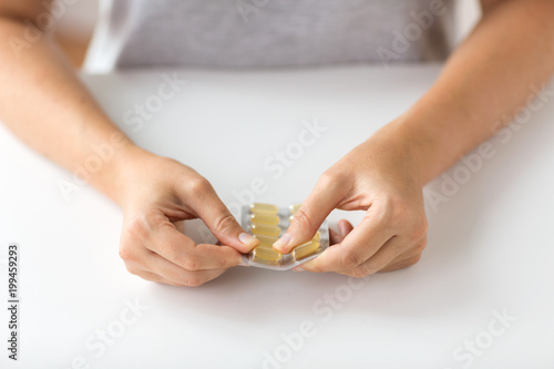 medicine, healthcare and people concept - woman hands opening pack of cod liver oil capsules