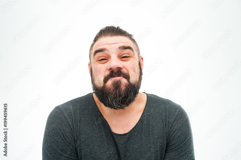 Good looking cute young bearded male looks with hesitant expression as doubts what to choose, points with thumb aside, copy space for promotional text or advertisment Good looking cute young bearded male looks with hesitant expression as doubts what to choose, points with thumb aside, copy space for promotional text or advertisment