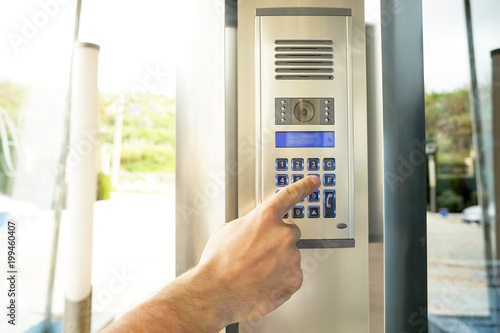 Close up of man hand entering security system code, pressing button with index finger on modern intercom device with blue lcd screen near entrence door. Male opens electronic code lock. Copy space. photo
