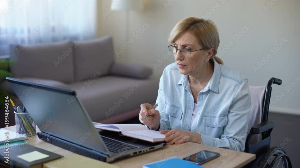 Handicapped grandmother making notes during online lesson home, senior student Handicapped grandmother making notes during online lesson home, senior student