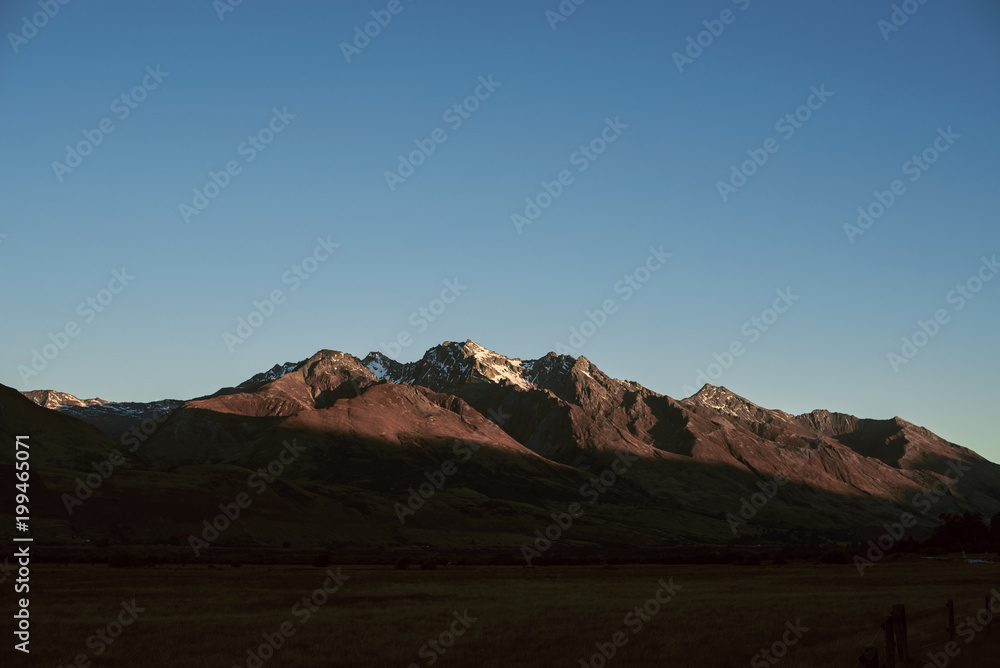 Paisaje de picos de montañas nevadas con cielo azul despejado al atardecer en Nueva Zelanda	