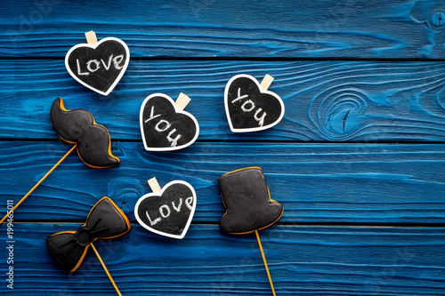 Happy Father's Day. Greetings and presents concept. Cookies in shape of moustache, hat, bow tie and hearts with lettering love you on blue wooden background top view copy space