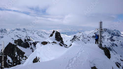 male backcountry skier at the summit cross of a high alpine peak on a beautiful winter day © makasana photo