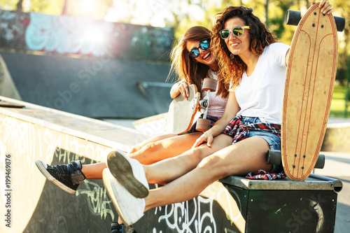 Two female skaters best friends hangout at the skate park on sunset .Laughing and fun.